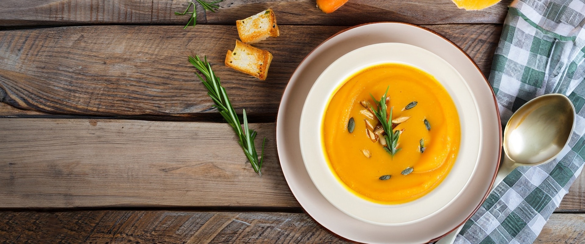 Pumpkin and carrot Cream soup on rustic wooden table. Autumn Pumpkin cream-soup with rosemary herb and croutons. Top view. Copy space.